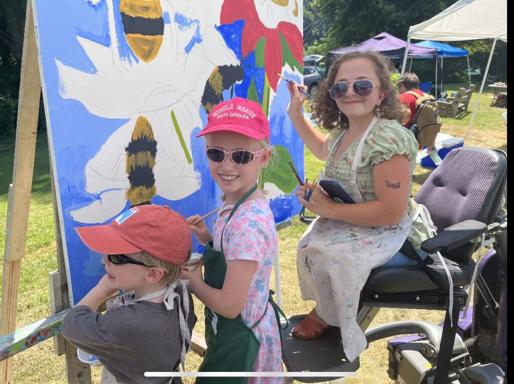 Three people paint a community mural during River Day
