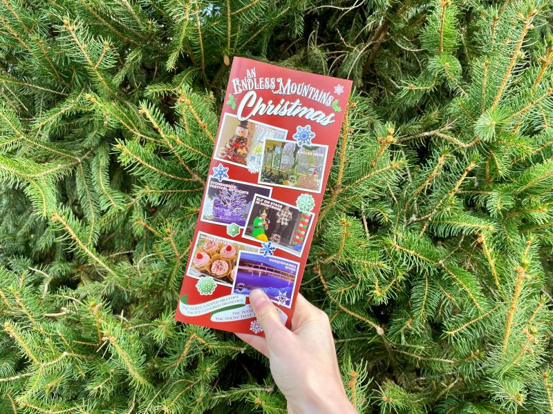 A red Endless Mountains Christmas brochure against a backdrop of pine boughs